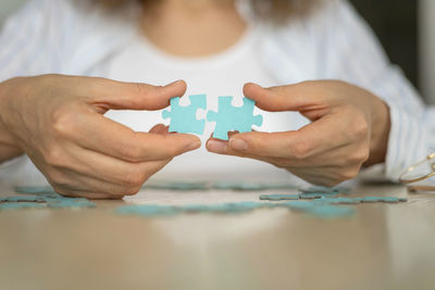 Midsection of woman holding jigsaw pieces on table