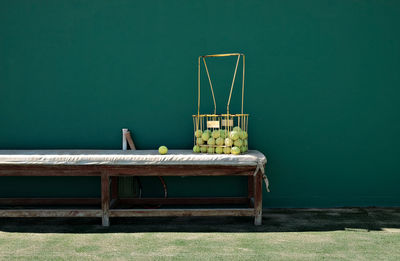 Tennis balls in metallic basket on bench against wall