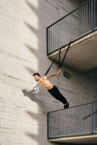 Young shirtless sportsman balancing on gymnastic rings outdoors