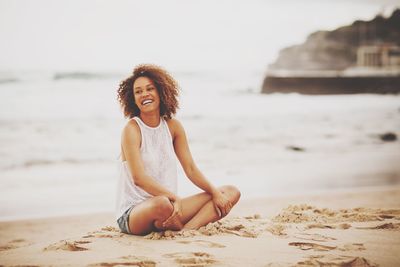 Cheerful young woman looking away while sitting at beach