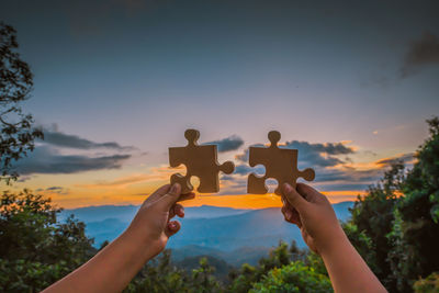 People holding hands against sky during sunset