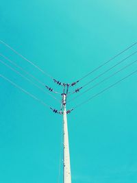 Low angle view of electricity pylon against clear blue sky during sunny day
