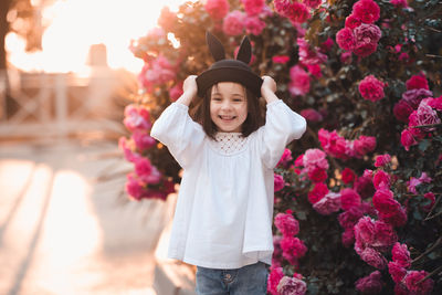 Cute stylish child girl 5-6 year old wear trendy clothes and hat posing over flower rose outdoor