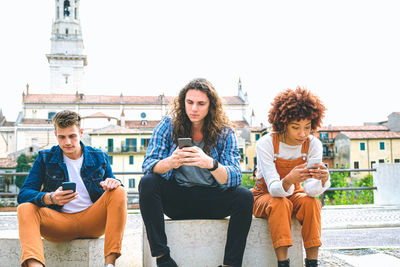 Friends using mobile phone sitting outdoors