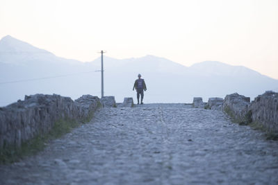 Rear view of man walking on mountain against sky