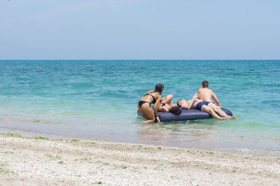 Men sitting on beach against clear sky