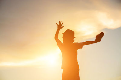 Silhouette woman with arms outstretched standing against sky during sunset