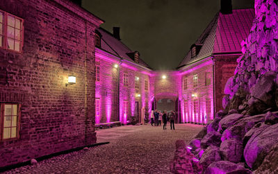 People walking on illuminated street amidst buildings at night