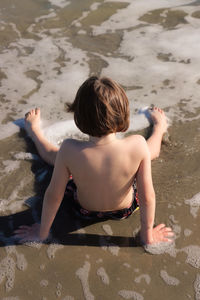 Rear view of shirtless boy sitting at beach