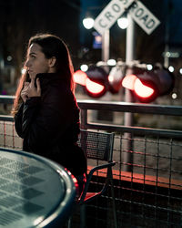 Thoughtful woman sitting at table against railroad crossing sign at night