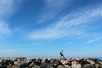 Man standing on rock against blue sky