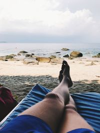 Low section of person relaxing on beach against sky
