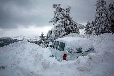 Snow covered car on snowcapped mountain against sky