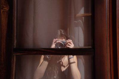 Reflection of woman photographing with camera seen in window