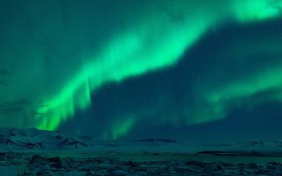 Aurora polaris over frozen landscape against sky