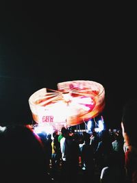 Illuminated carousel in amusement park against sky at night