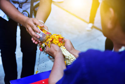 Midsection of man pouring water on flowers held by friend during wedding ceremony