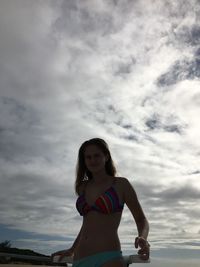 Portrait of teenage girl wearing bikini standing against cloudy sky