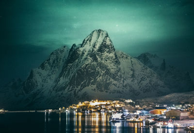 Scenic view of sea by snowcapped mountains against sky at night