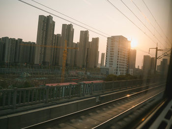 Railroad tracks by buildings in city against sky during sunset