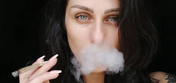 Portrait of woman smoking cigarette against black background