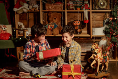 Two real brothers lie in a room with new year's decor near an armchair and look at gifts