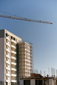 Low angle view of crane by building against clear sky