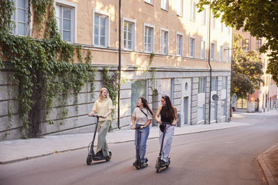 Young female friends spending time together outdoors riding electric scooters