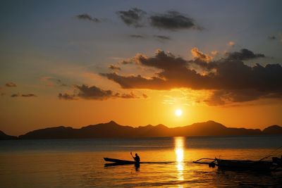 Silhouette people in sea against sky during sunset