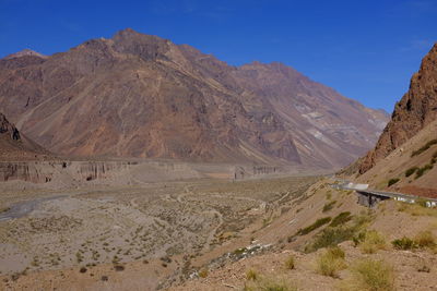 Scenic view of road by mountains against clear blue sky