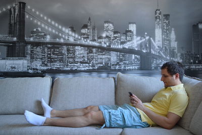 Side view of man reclining on sofa while using mobile phone against picture frame at home