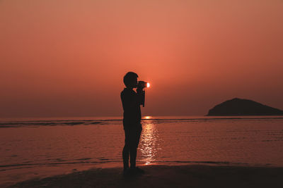 Silhouette man standing on beach against sky during sunset