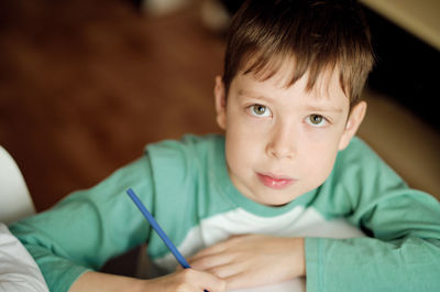 Cute and smiling cucasian boy draws with colored pencils while sitting at the table