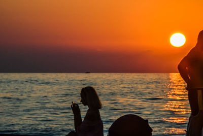 Woman by sea against sky during sunset