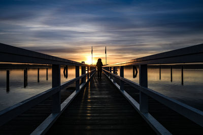 Man on footbridge against sky during sunset