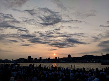 Group of people in city against sky during sunset