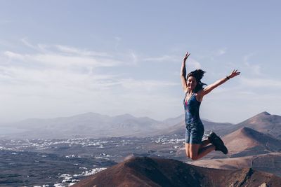 Full length of young woman with arms raised against sky