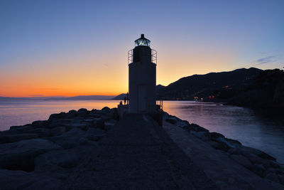 Lighthouse by sea against sky during sunset