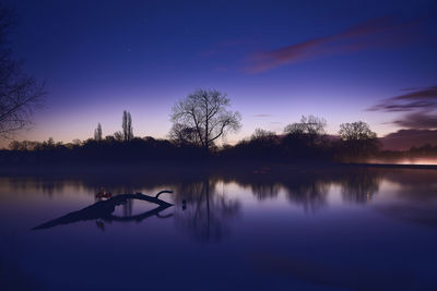 Silhouette trees by lake against sky during sunset