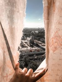 Cropped image of hand against buildings in city