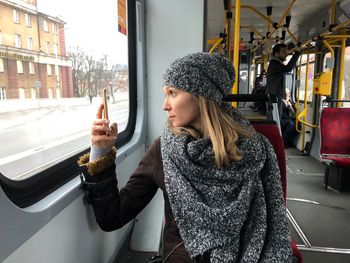 Mid adult woman photographing with mobile phone while traveling in bus