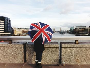 Low section of woman holding british flag umbrella while standing on bridge by thames river