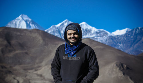 Portrait of young man standing on snowcapped mountain against sky