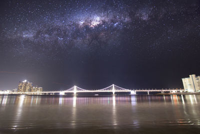Illuminated bridge over river against sky in city at night