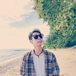 Portrait of young man standing at beach against sky during sunset
