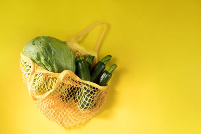 Top view of mesh shopping bag with organic eco green vegetables isolated on yellow background