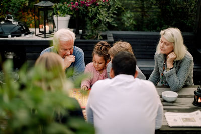 Multi-generation family playing board game on table while sitting in patio