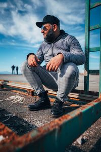 Man sitting on old rusty metal against sky