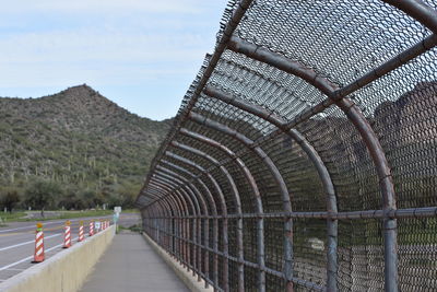 Walkway by fence against sky