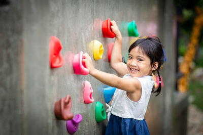 Happy girl holding multi colored standing against wall